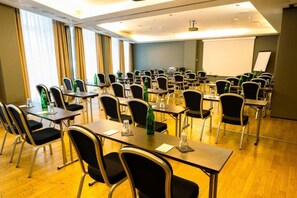 Ein Konferenzraum mit Tischen, Stühlen, einer Projektionsleinwand und einem großen Fenster mit Vorhängen.