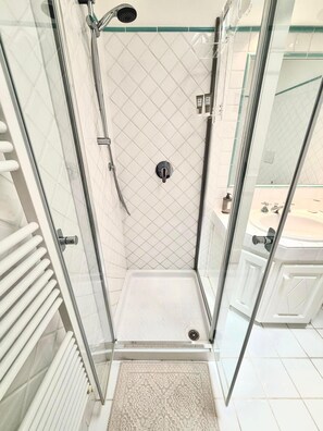 Ducha con mampara de vidrio, cabezal de ducha de mano, panel de control y pared revestida de azulejos blancos.