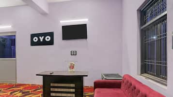 Una habitación con un sofá rojo, una mesita, un televisor instalado en la pared y un letrero que dice 'OYO'.