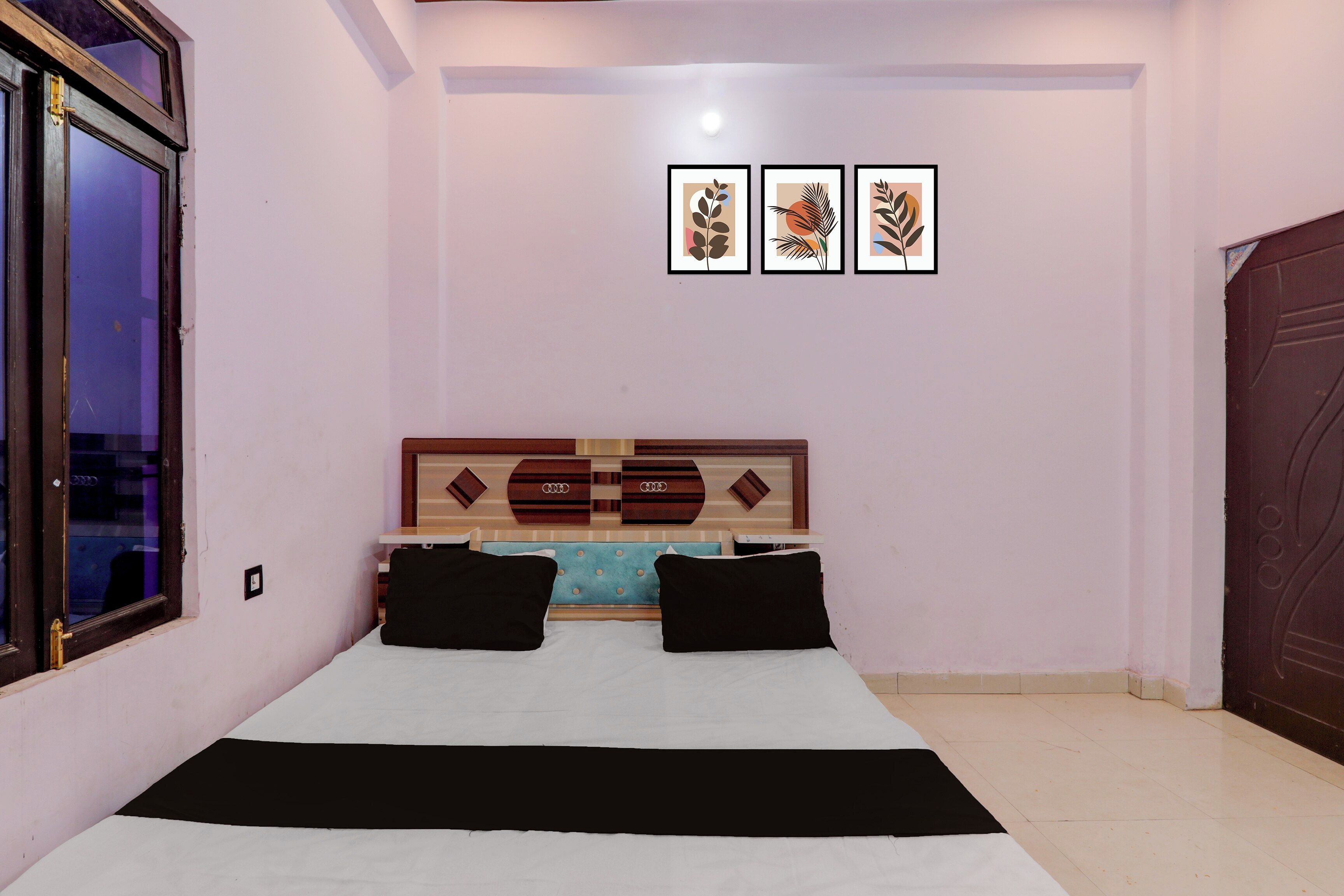 Quarto com cama, cabeceira com painéis decorativos e três obras de arte emolduradas na parede.
