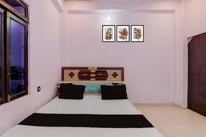 Quarto com cama, cabeceira com painéis decorativos e três obras de arte emolduradas na parede.