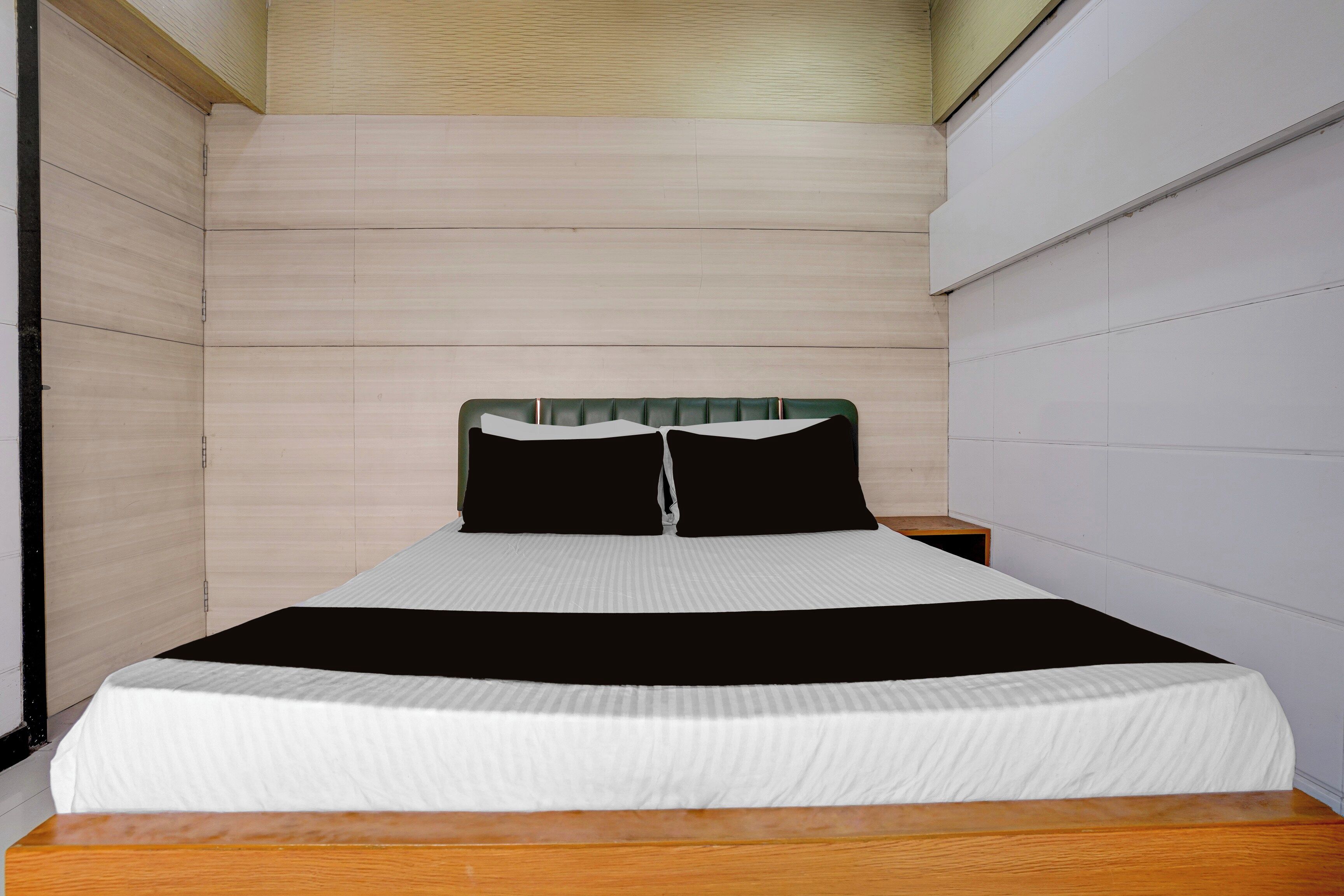Una cama individual con cabecera de madera, cubrecama a rayas blancas y negras, y suelo de madera.