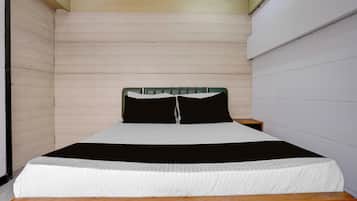 Una cama individual con cabecera de madera, cubrecama a rayas blancas y negras, y suelo de madera.
