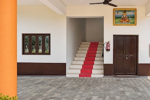 A staircase with red steps leading to a dark wooden door, a fire extinguisher mounted on the wall, and a framed picture above the door. - Hotel O SMD Grand Resort (Misrikh)