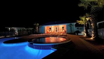 A swimming pool with a circular edge, a building with a porch and chairs, and palm trees.