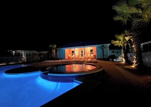 A swimming pool with a circular edge, a building with a porch and chairs, and palm trees. - Charming Beachside Retreat with Pool Views in Gulf Shores (Gulf Shores)