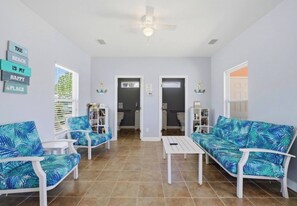 A living room with two white sofas, a coffee table, and a ceiling fan. There are two doors leading to other rooms. - Charming Beachside Retreat with Pool Views in Gulf Shores (Gulf Shores)
