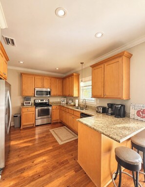 A kitchen with wooden cabinets, stainless steel appliances, a granite countertop, and a bar stool. - Charming Beachside Retreat with Pool Views in Gulf Shores (Gulf Shores)