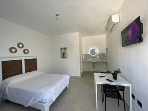 Una camera d'albergo con un letto, una scrivania, una sedia, uno specchio e una TV a parete.