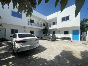 Ein zweistöckiges Gebäude mit weißer Fassade, einer blauen Tür und einem Parkplatz mit zwei Autos.
