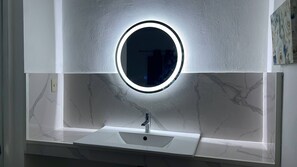 Un bagno con uno specchio rotondo, un lavandino e una parete in marmo.
