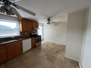 Une cuisine avec des meubles de rangement en bois, une cuisinière, un lave-vaisselle et un ventilateur de plafond.