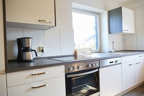 A modern kitchen with white cabinets, a built-in oven, a coffee maker, and a window providing natural light. - Holiday home in Rimsting with swimming pool (Rimsting)