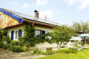A house with a sloped roof, solar panels, a chimney, and a garden with a bench and lounge chairs. - Holiday home in Rimsting with swimming pool (Rimsting)
