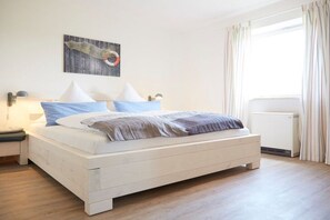 A bedroom with a bed, a nightstand, a wall-mounted lamp, and a window with curtains. - Holiday home in Rimsting with swimming pool (Rimsting)
