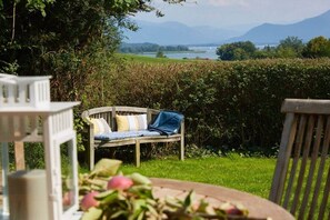 A garden with a wooden bench and a table, surrounded by greenery and a view of a lake and mountains. - Holiday home in Rimsting with swimming pool (Rimsting)