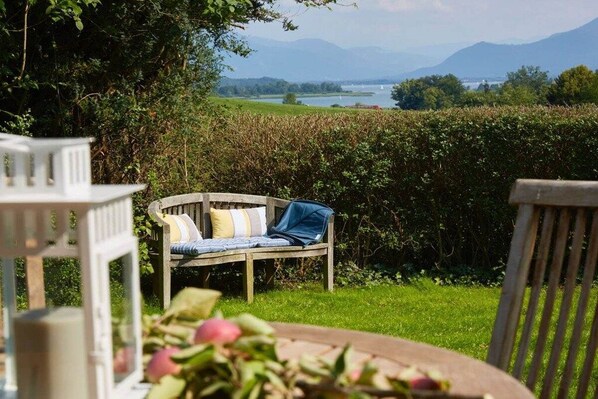 A garden with a wooden bench and a table, surrounded by greenery and a view of a lake and mountains. - Holiday home in Rimsting with swimming pool (Rimsting)
