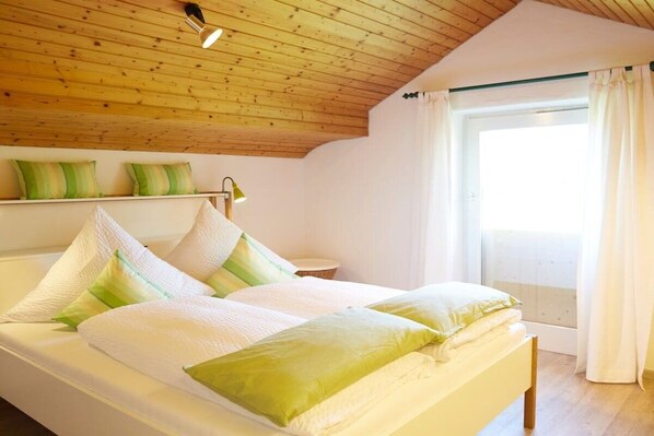 A bedroom with a wooden ceiling, a bed with white and green bedding, a bedside table with a lamp, and a window with curtains. - Holiday home in Rimsting with swimming pool (Rimsting)