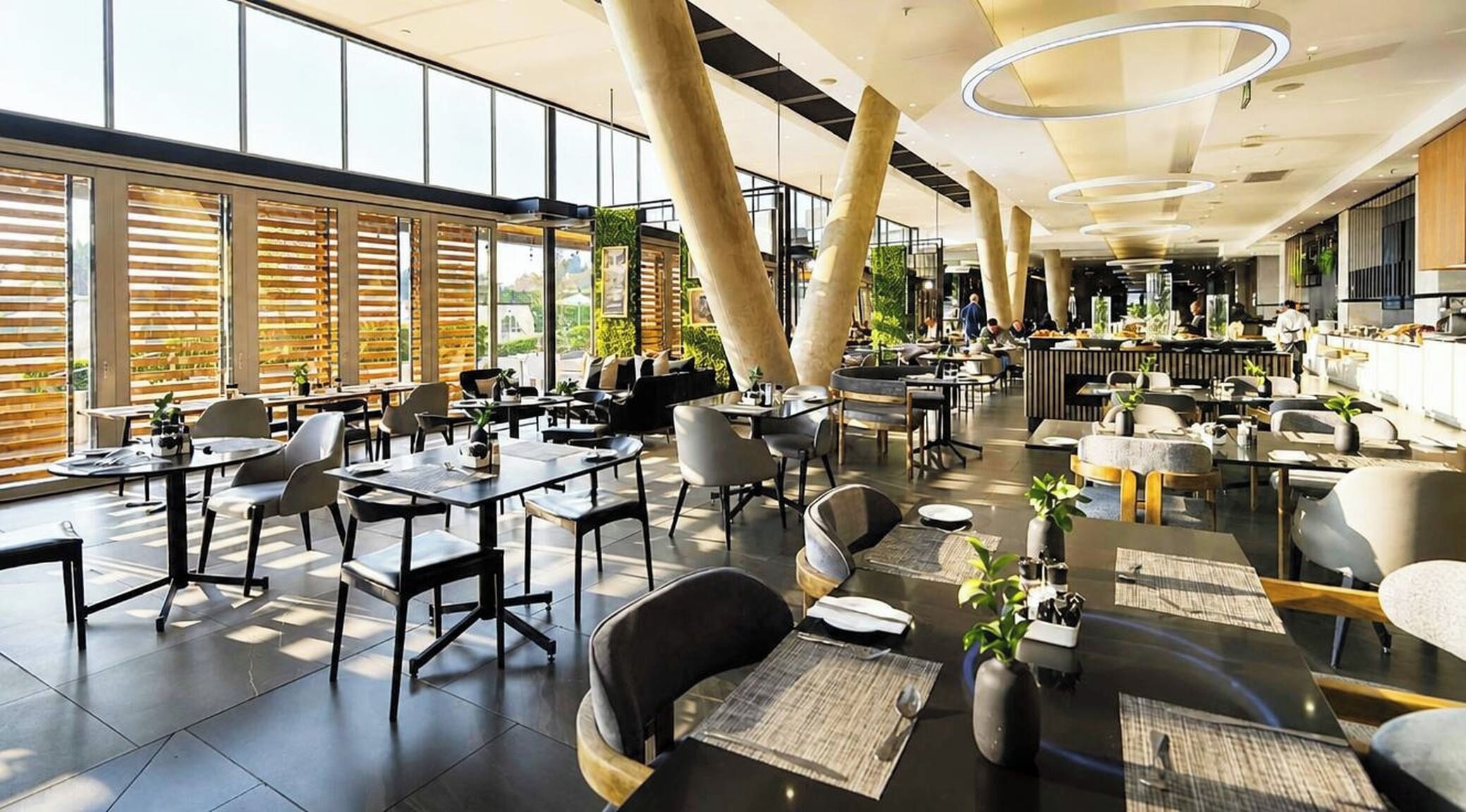 A spacious indoor area with multiple seating arrangements, including tables and chairs, and large windows allowing natural light.