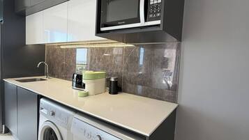 A compact kitchen with a washing machine, a microwave, and a built-in oven.