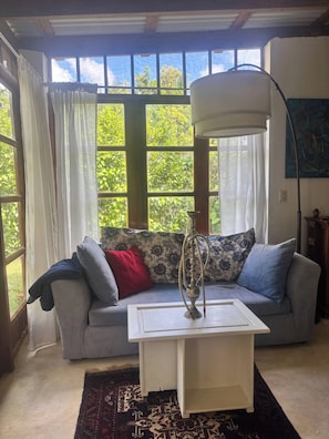 A room with a sofa, a coffee table, and a lamp. There are windows with curtains, and a painting on the wall. - CB Tropical paradise (Cabrera)