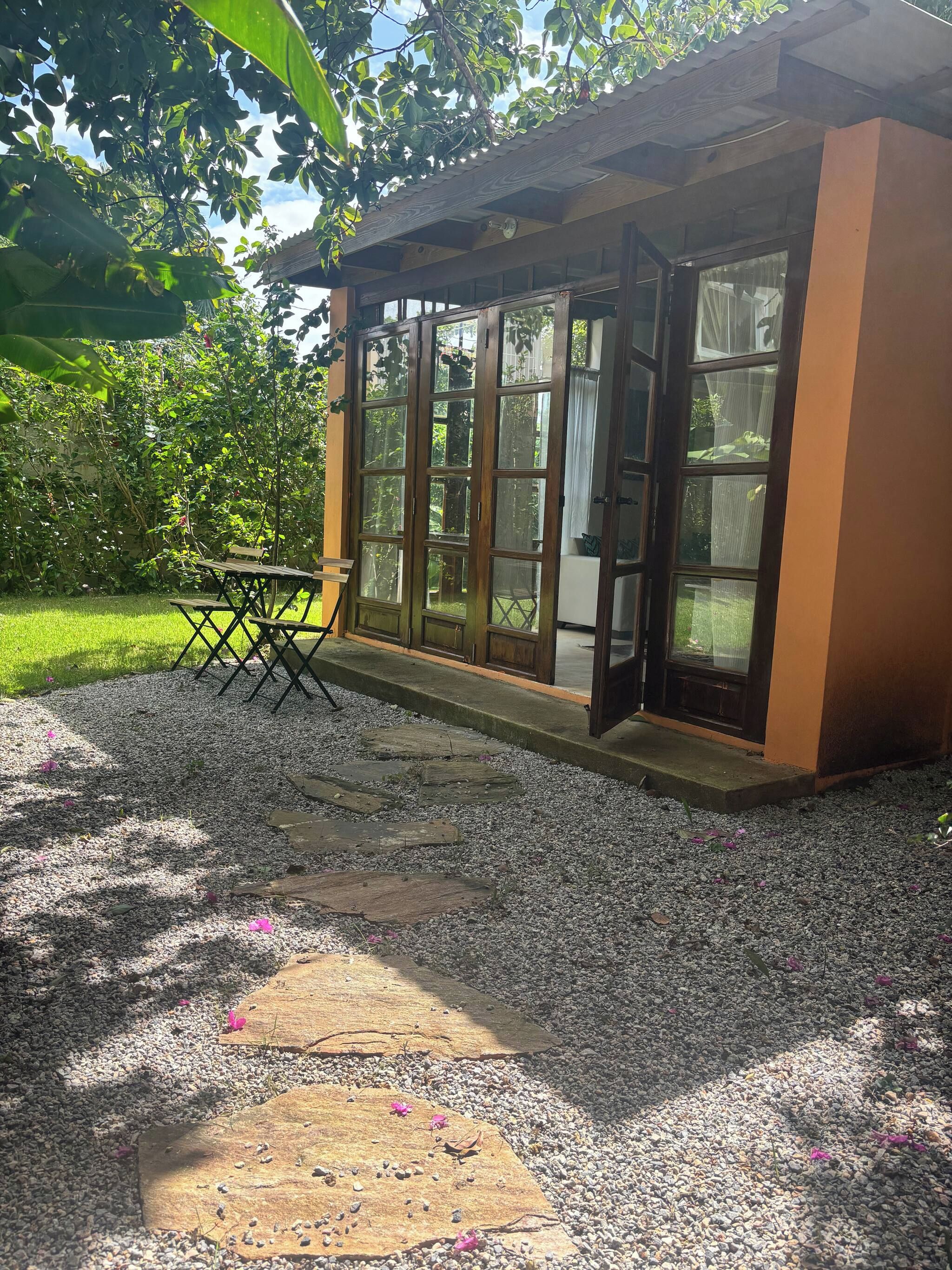 Un espace extérieur aménagé, abrité et doté d’une table et de chaises, entouré d’un chemin de gravier et de verdure.