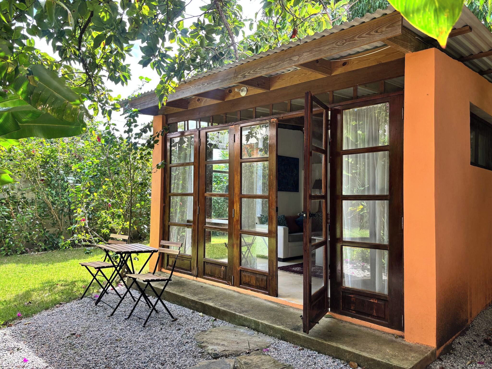 Une structure en bois dotée de grandes portes vitrées, d’une zone recouverte de gravier et d’une table avec des chaises.