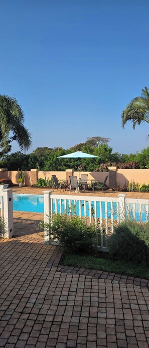 Un espace piscine avec une terrasse en briques, des chaises longues et une table avec un parasol.