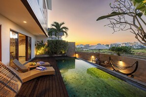 Un'area piscina sul tetto con sedie a sdraio, un'amaca e vista sulla città al tramonto.
