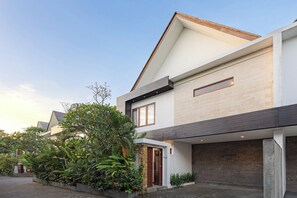 Una casa moderna a due piani con tetto piatto, un garage e un giardino curato con diverse piante e fiori.