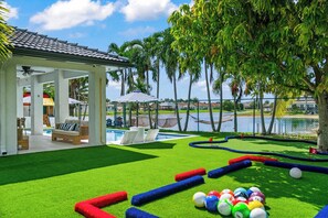 Un área de piscina con césped artificial, una zona de estar con sofá y sillones, y un pabellón.