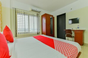 Ein Hotelzimmer mit Bett, Schreibtisch, Stuhl, Fernseher und einem Fenster mit Jalousien.