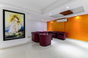 Un interior moderno con un cuadro grande enmarcado, una zona de estar con sillas moradas y un equipo de aire acondicionado en la pared.