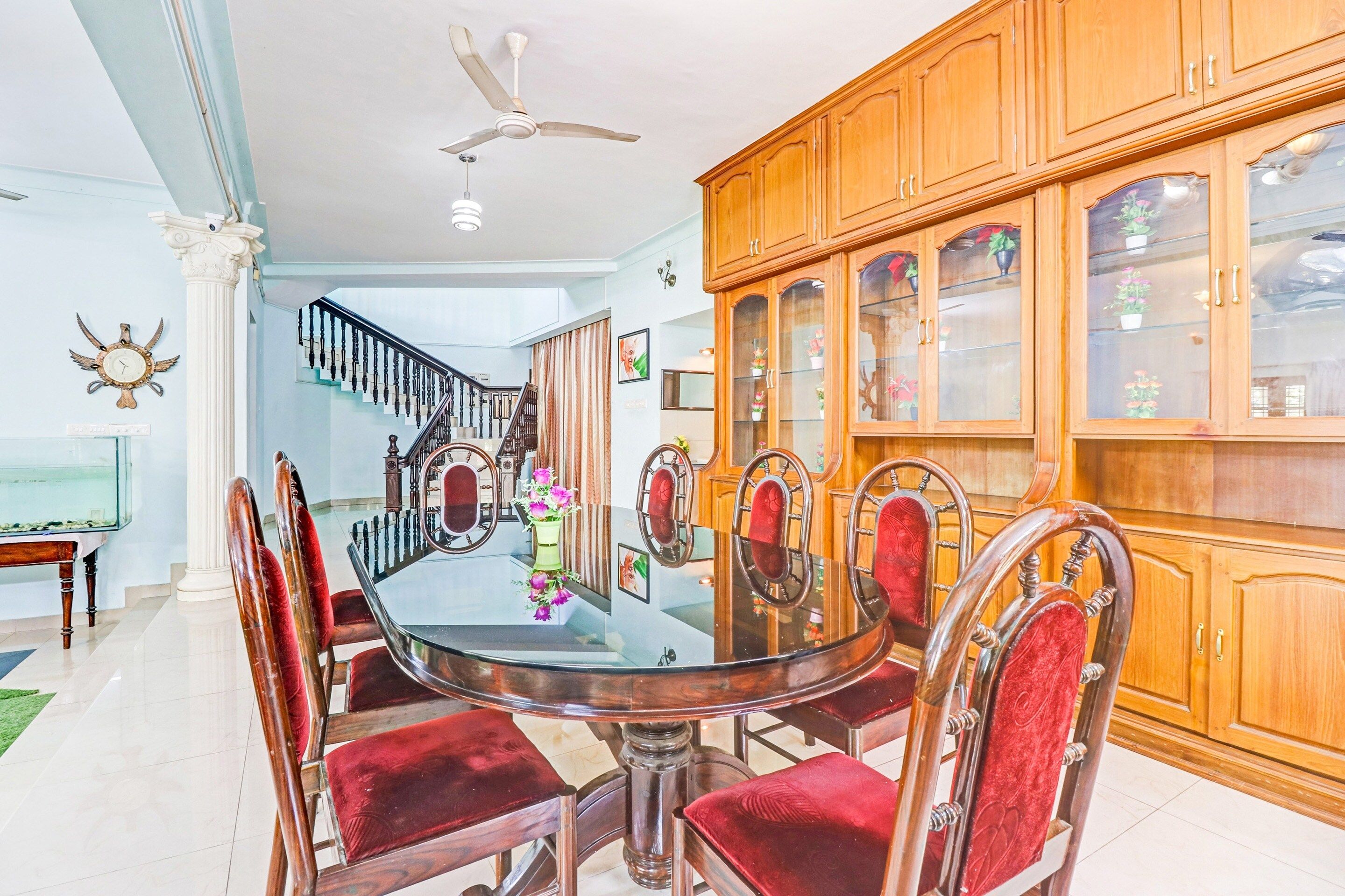 Un comedor con una mesa redonda de vidrio, sillas tapizadas rojas y un mueble de madera con puertas de cristal.