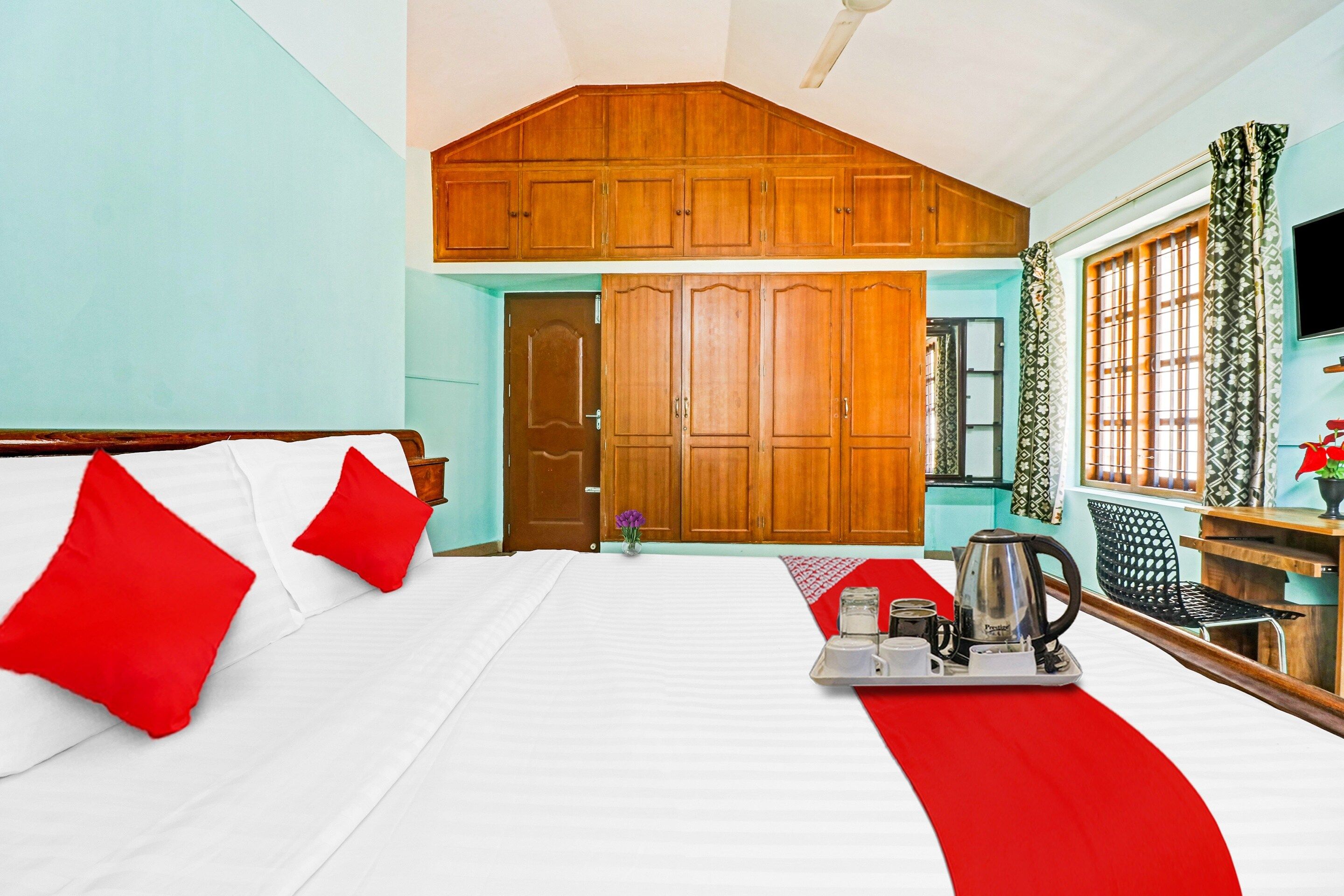 Une chambre d’hôtel avec un lit, un bureau doté d’une bouilloire, une fenêtre avec des rideaux et une armoire en bois.
