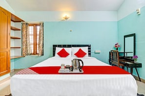 Une chambre d’hôtel comprenant un lit, un bureau, une chaise, une fenêtre avec des rideaux et un luminaire fixé au mur.