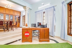 Une pièce comprenant un bureau en bois, une chaise, un meuble avec des portes en verre et une grande fenêtre avec des rideaux.