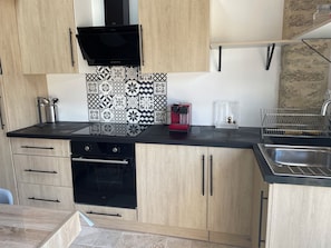 Une cuisine moderne avec des meubles en bois, une cuisinière noire, une machine à café rouge et un dosseret carrelé.