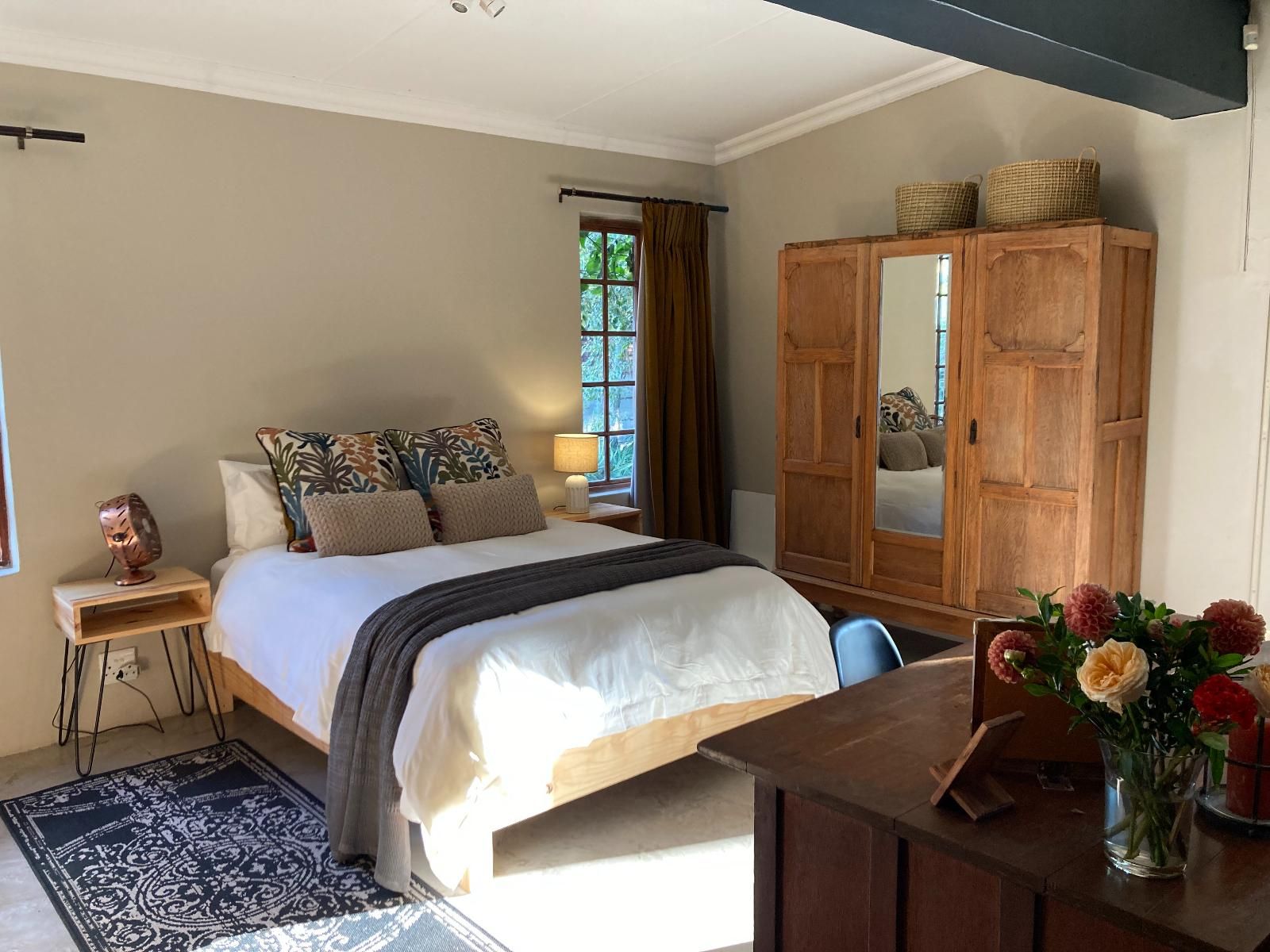 Un dormitorio con cama, mesita de noche, lámpara, armario y un escritorio con un jarrón de flores.