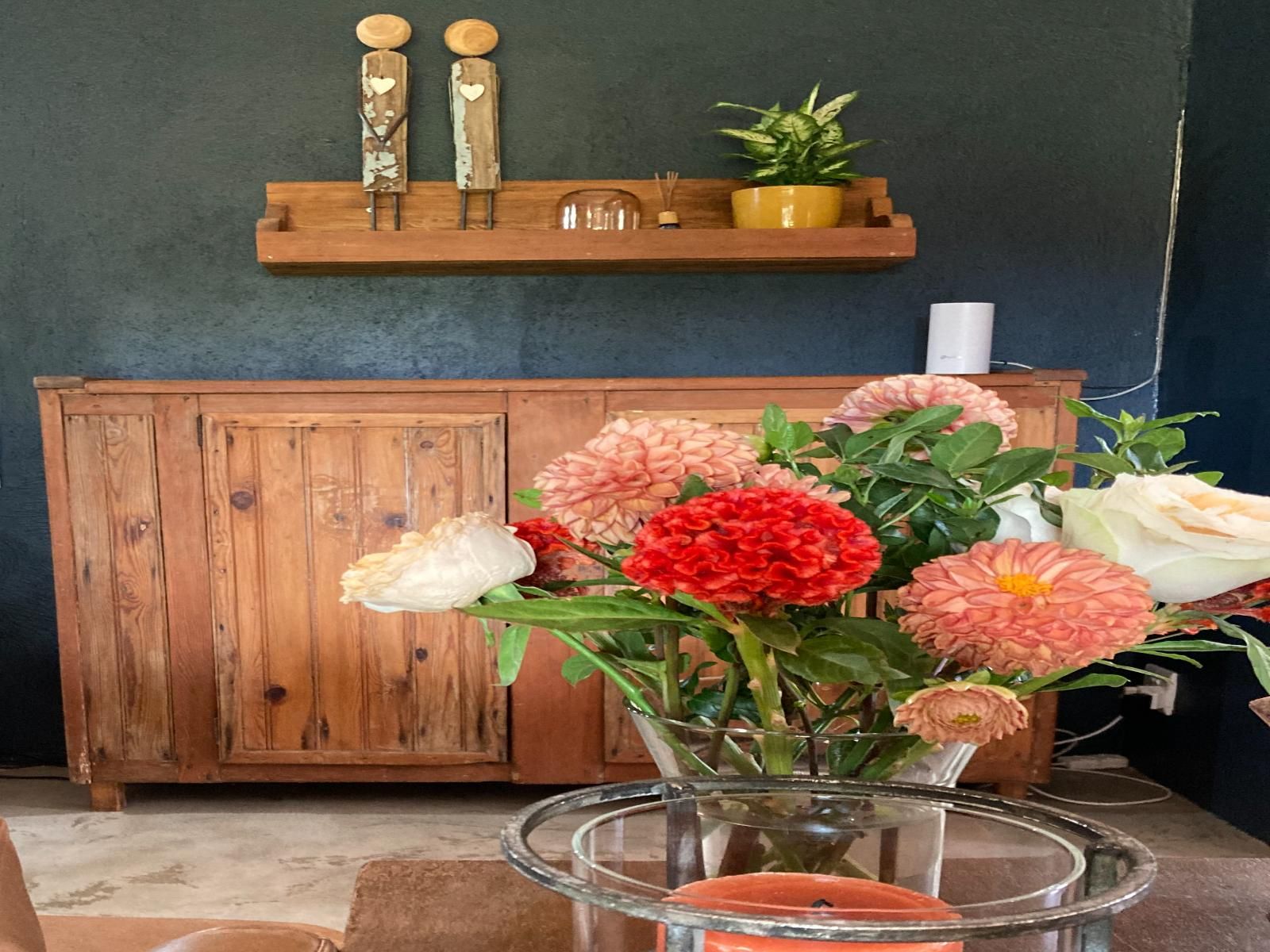 A wooden cabinet with a shelf above it, a glass vase with flowers, and a potted plant on the shelf.