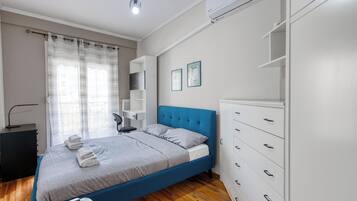 A bedroom with a bed, a desk, a chair, a wardrobe, and an air conditioning unit.