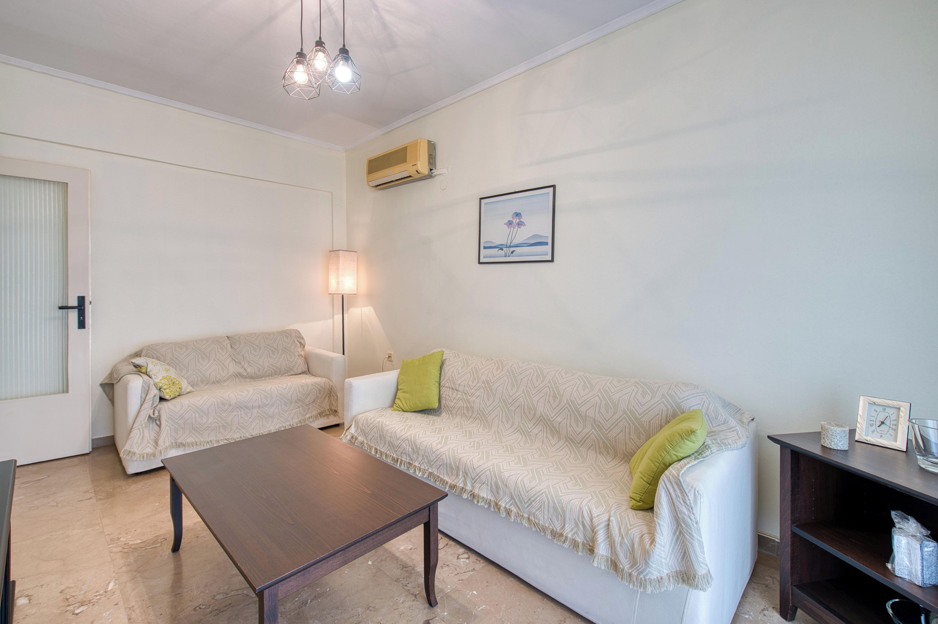A living room with a sofa, a coffee table, a lamp, and a wall-mounted air conditioner.