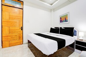 Une chambre avec une porte en bois, un lit avec une literie noire et blanche, une table de chevet avec une lampe et un tableau accroché au mur.