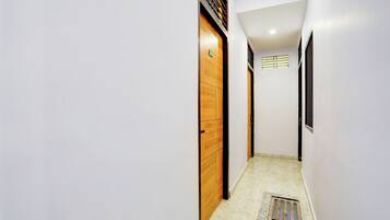 Um corredor estreito com uma porta de madeira, uma janela com persianas e um cano de esgoto no chão.