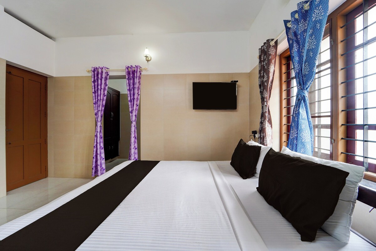 Een hotelkamer met een bed, een flatscreen televisie aan de muur, een raam met gordijnen en een deur.