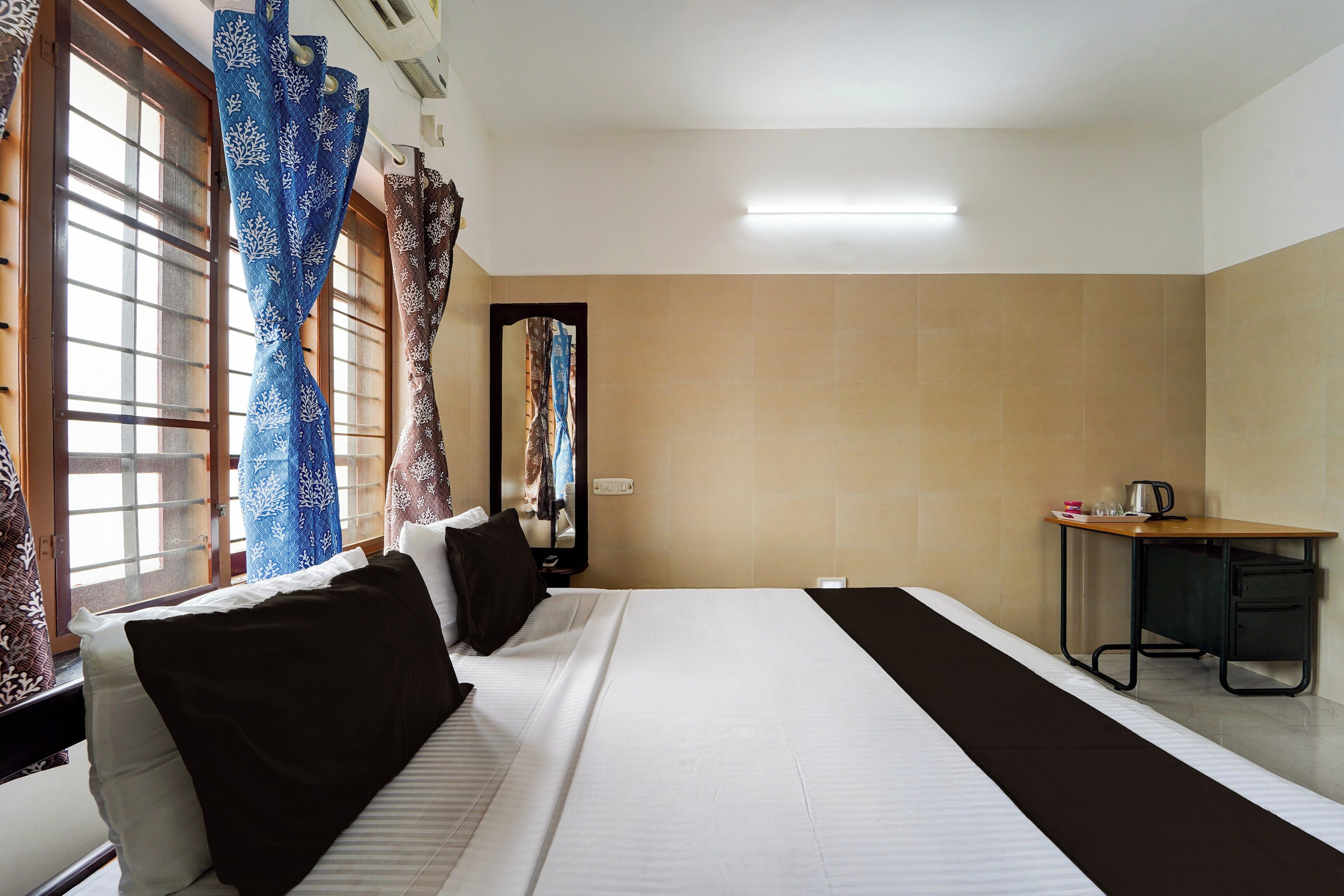 A hotel room with a bed, a desk, a mirror, and a window with curtains.
