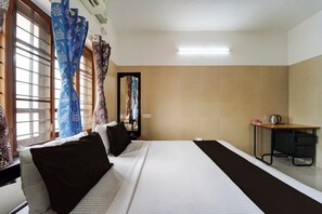 Een hotelkamer met een bed, een bureau, een spiegel en een raam met gordijnen.
