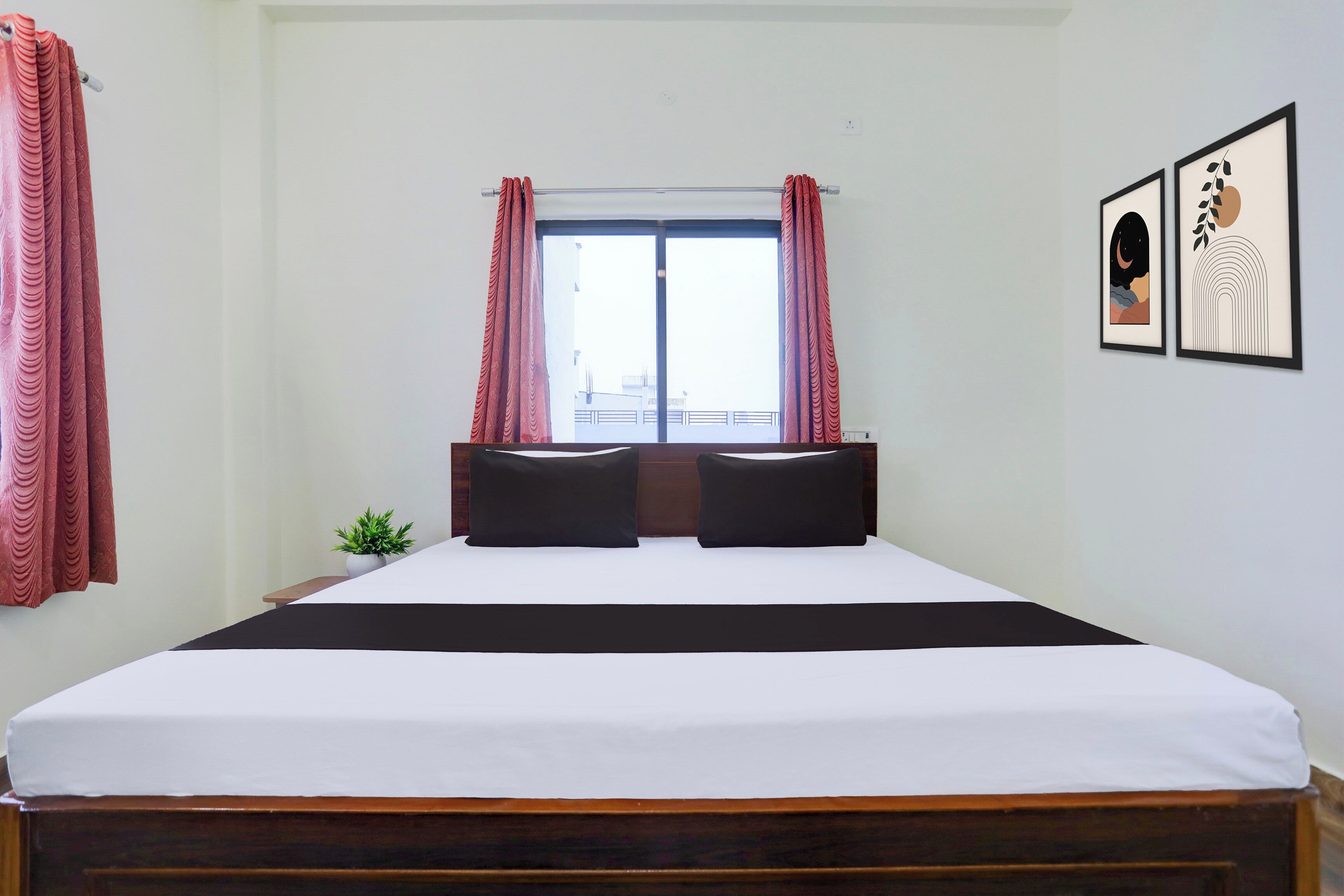 Une chambre d’hôtel avec un grand lit, deux oreillers, une petite plante et une fenêtre avec des rideaux.