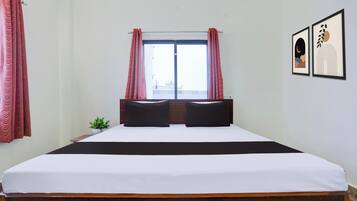 Une chambre d’hôtel avec un grand lit, deux oreillers, une petite plante et une fenêtre avec des rideaux.