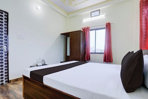 Une chambre d’hôtel comprenant un lit, une armoire, une fenêtre avec des rideaux et une petite table avec une bouilloire et des tasses.